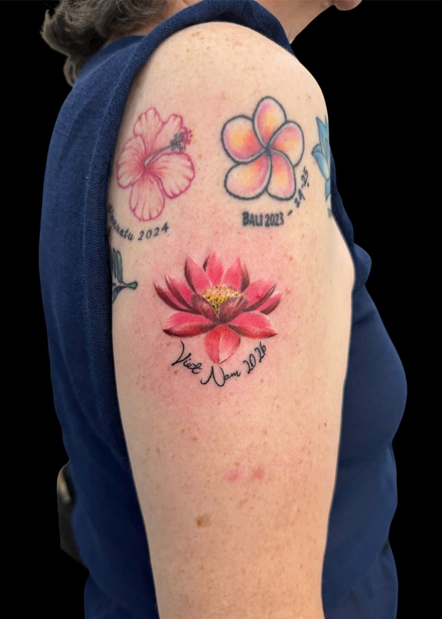 Colour realism lotus and frangipani floral arm tattoo with Vietnam script — Rae Ink Saigon