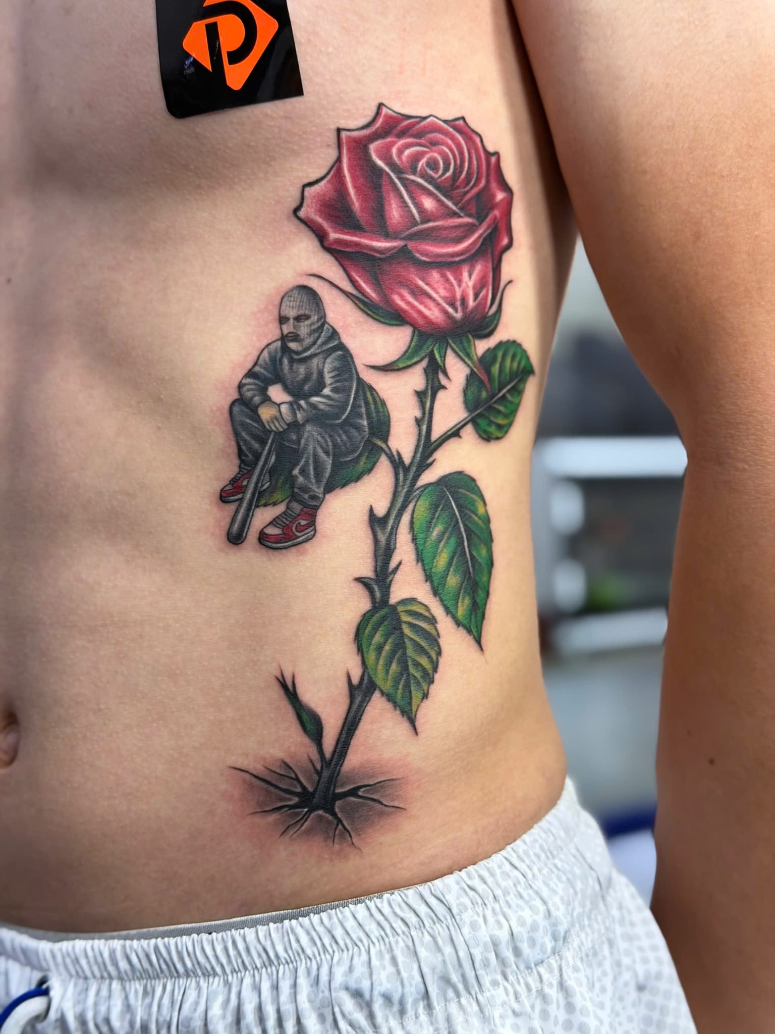 Colour rose with seated figure ribs tattoo — Rae Ink Saigon